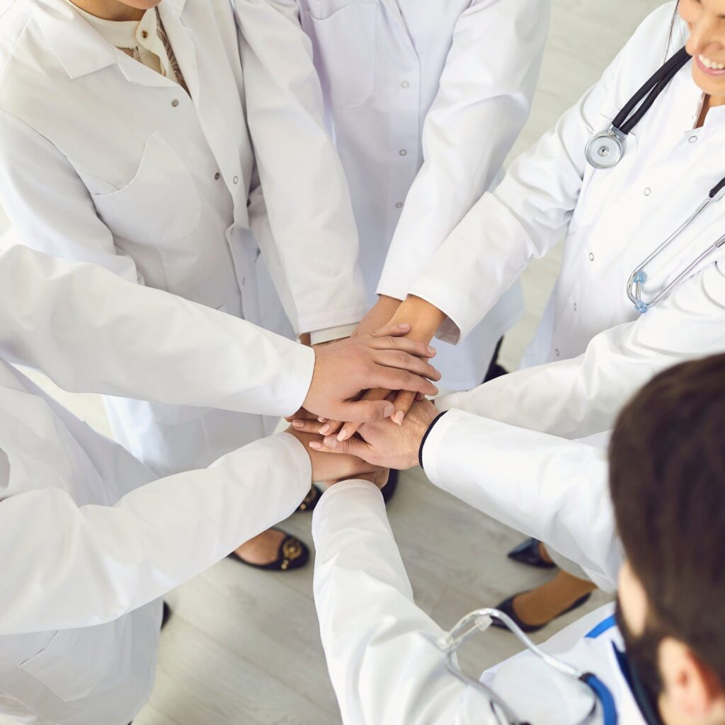 A group of medical professionals in white lab coats placing their hands together in a team gesture, symbolizing unity.