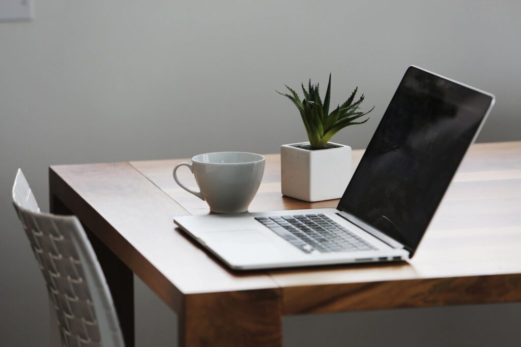 A minimalist workspace with a laptop, a coffee cup, and a small potted plant on a wooden table.