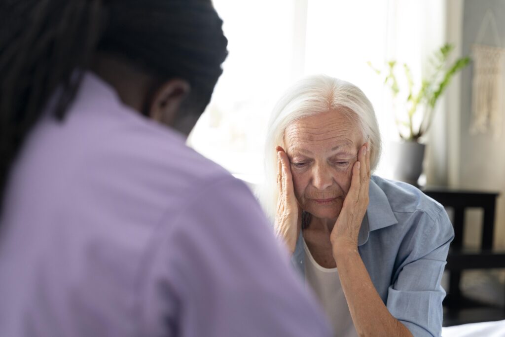 An elderly woman looking confused with her head in her hands, sitting across from a social worker during a conversation