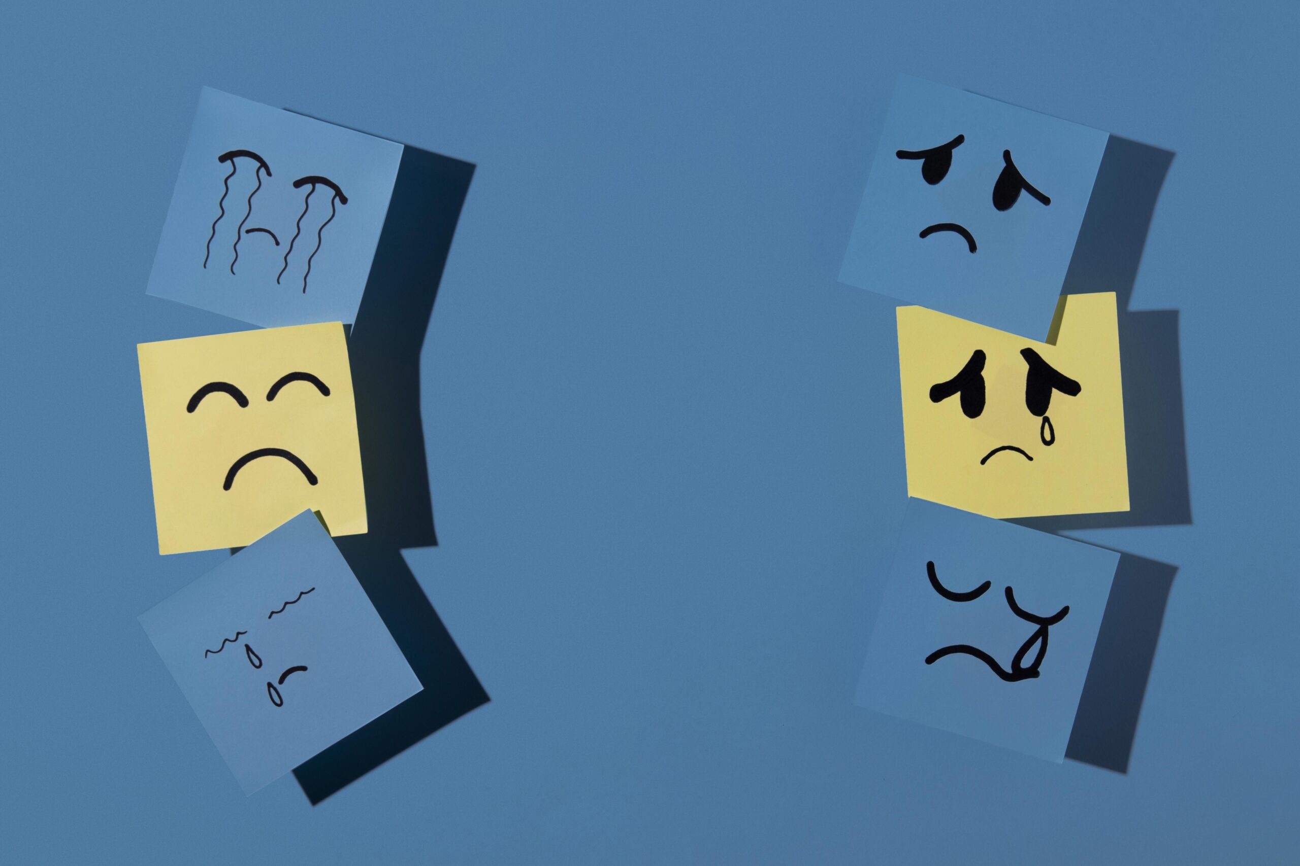 A collection of sad face drawings on sticky notes. The notes are arranged in two vertical columns against a blue background, showing different emotional expressions.