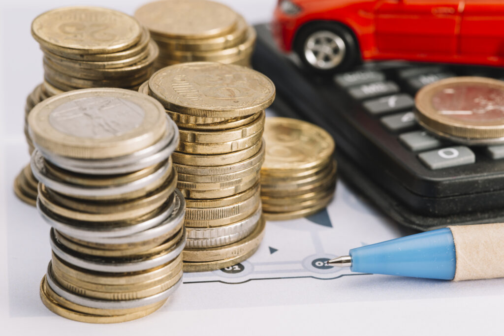 A close-up image of stacked gold and silver coins next to a blue pen and a calculator.