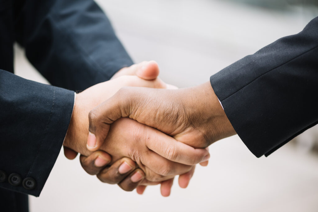 A close-up of two people shaking hands, both wearing dark suits.