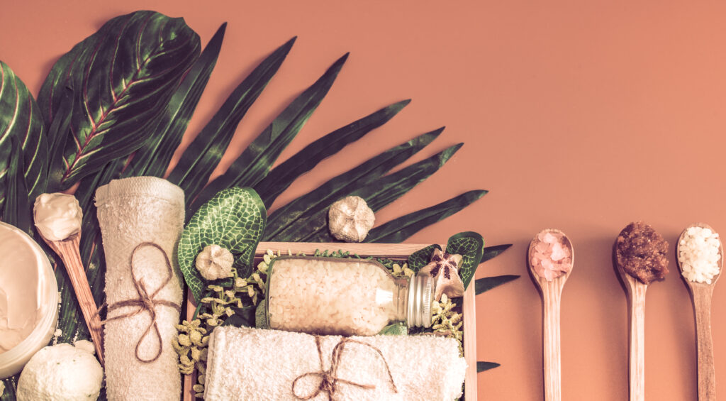 A spa-themed arrangement with towels, bath salts, and natural decorations displayed on a brown surface with palm leaves