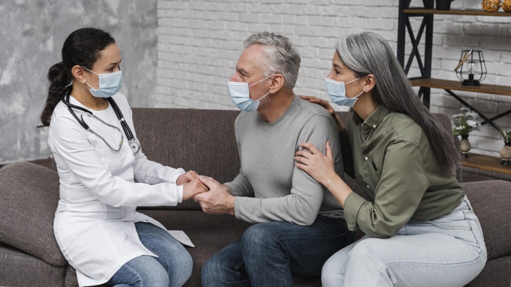 A doctor holding hands with a senior man while a supportive woman sits beside him