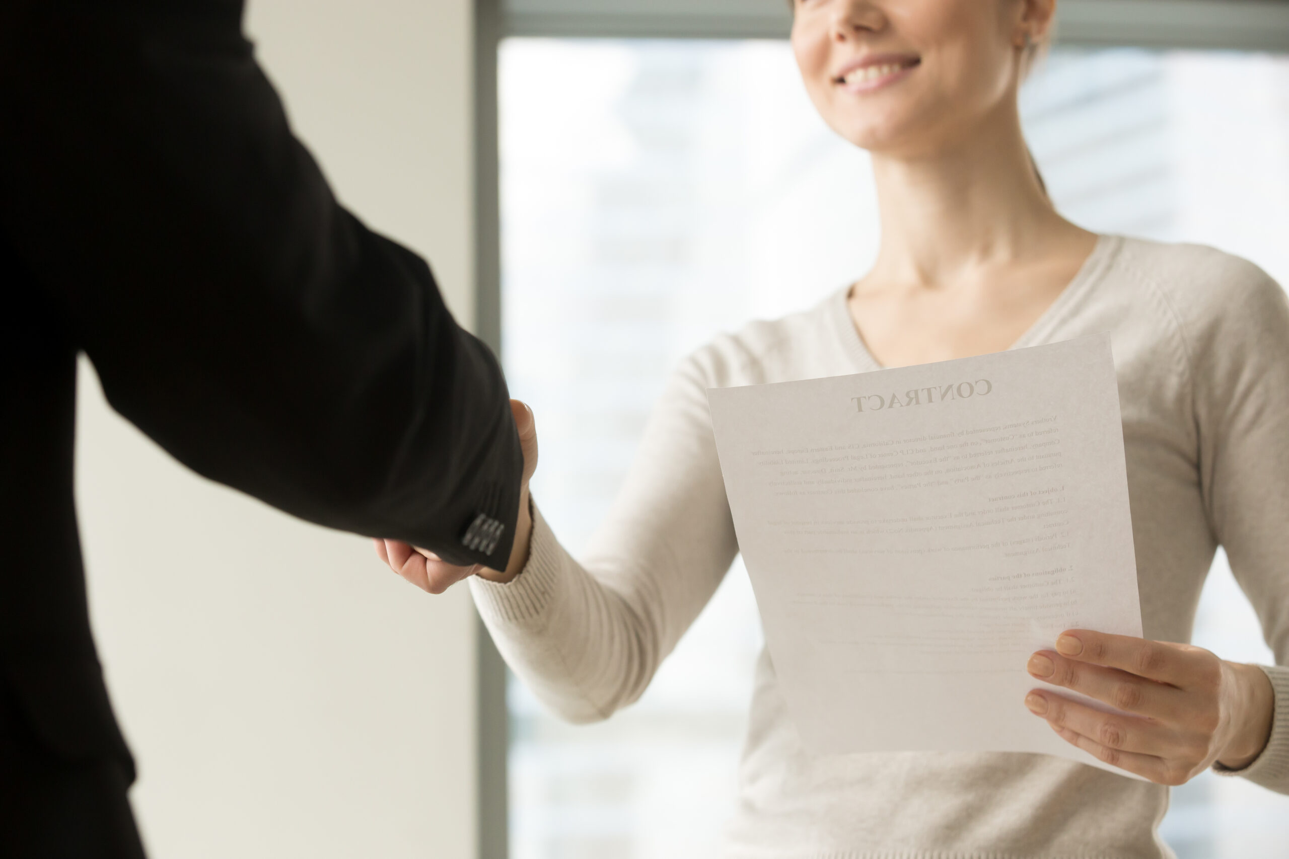 A woman holding a contract and shaking hands with a person in a business suit.