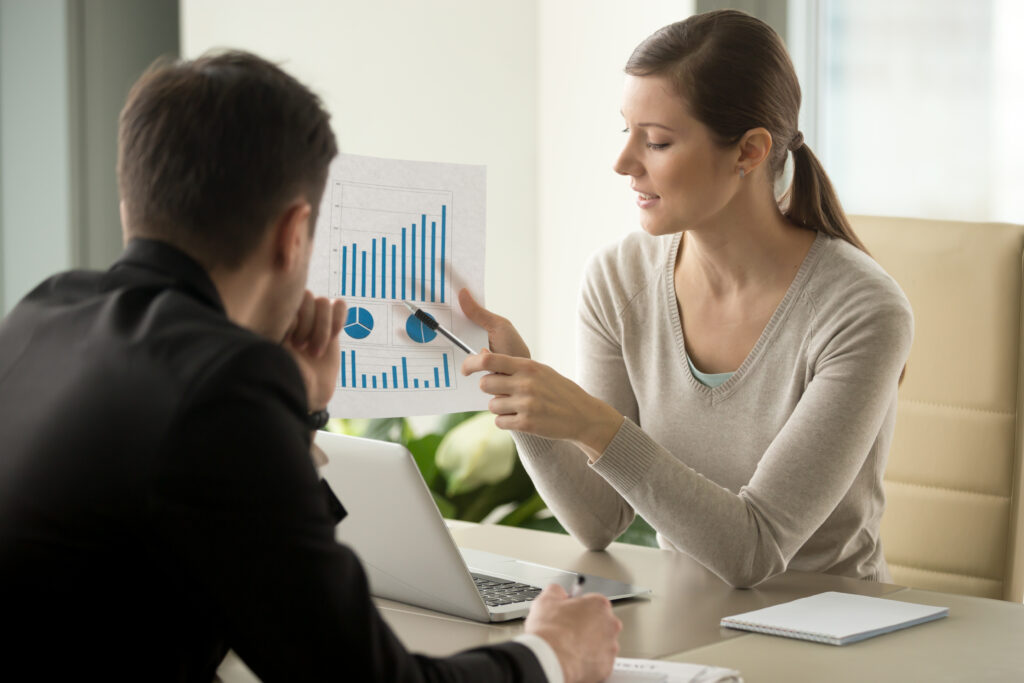 A woman presenting a document with charts and graphs to a man in a business meeting, explaining data or a business plan.