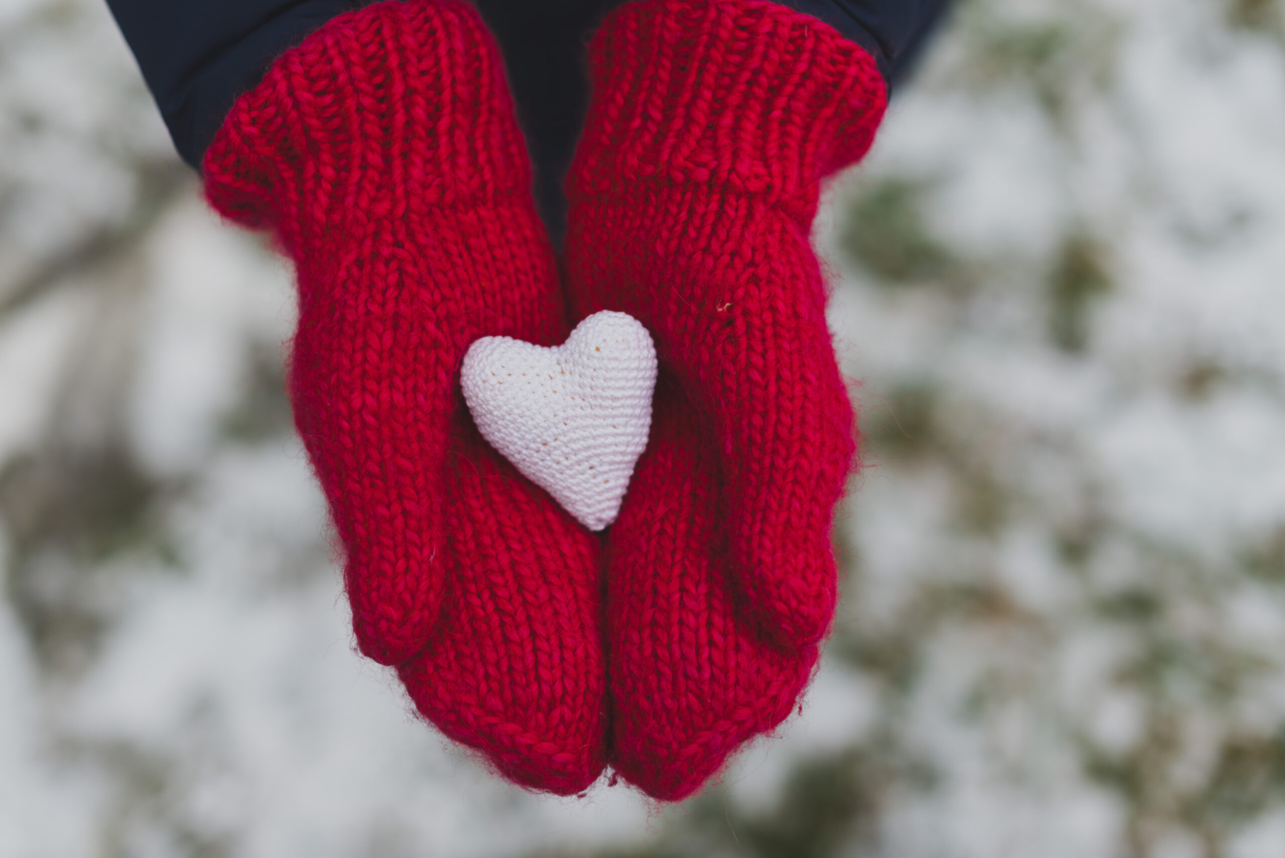 Red mittens holding a small white heart in a snowy setting.