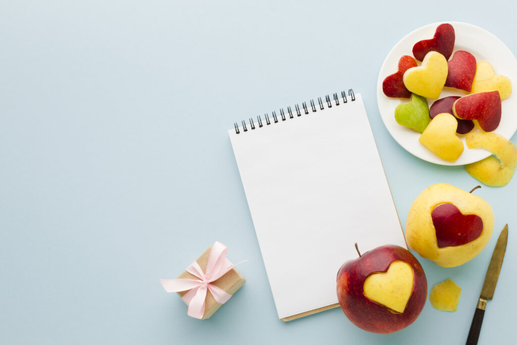 A blank notepad with heart-shaped apple slices, a small gift box, and a knife.