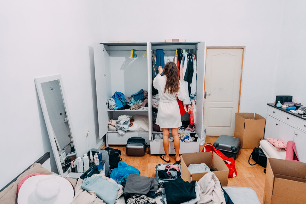 A woman organizing clothes in an open wardrobe, with suitcases and boxes scattered around the room