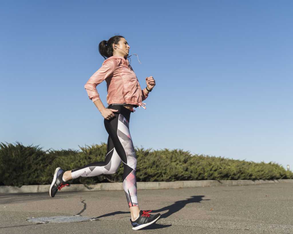 A woman jogging outdoors on a sunny day, wearing athletic wear.