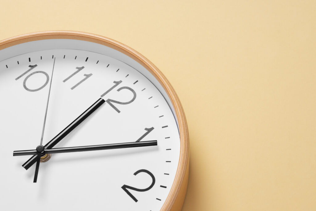 A close-up of a wall clock with a minimalist design on a light beige background.