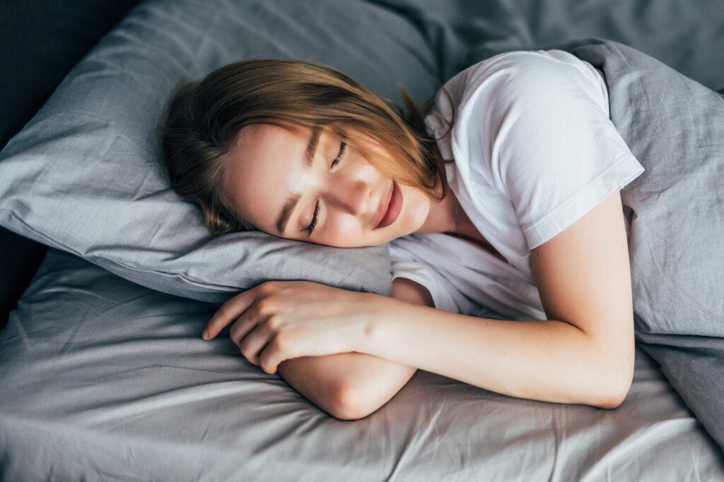 A young woman peacefully sleeping on a grey bed, with a relaxed expression.